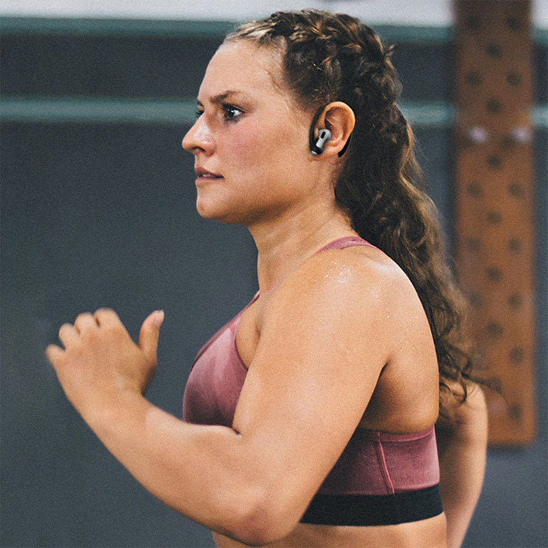 A woman that is jogging or running, in a sports bra, wearing black Atomical AirPod Pro accesories.