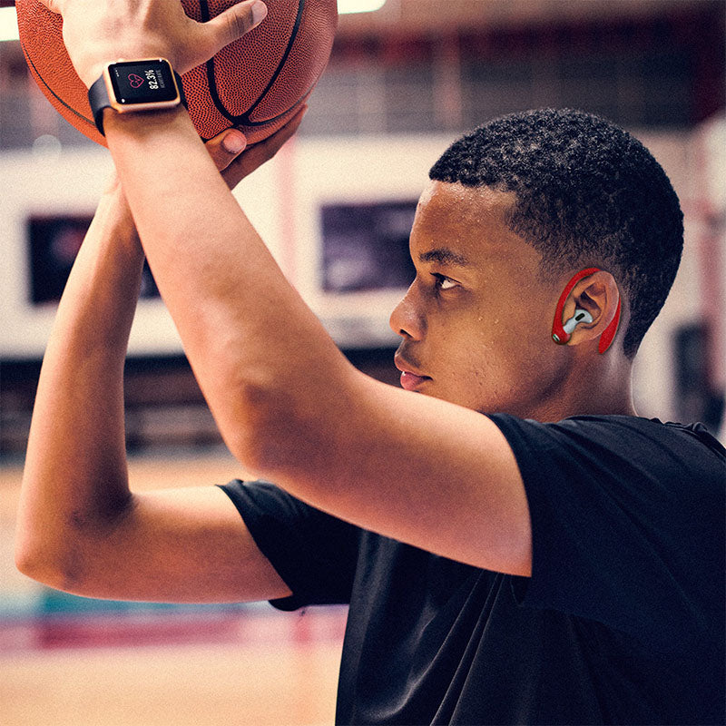 A young man or a teen playing basketball, while wearing apple products and accesories, as well as red AirPod pro Earhooks.
