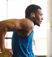 A man exercising, doing dips at the gym, and is wearing white AirPod Earhooks.